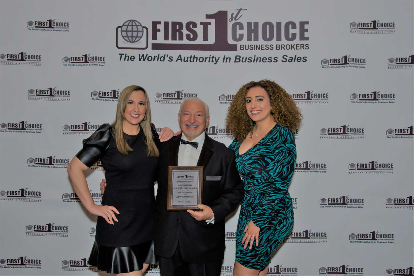 A man and two women are standing next to each other in front of a wall that says first choice.