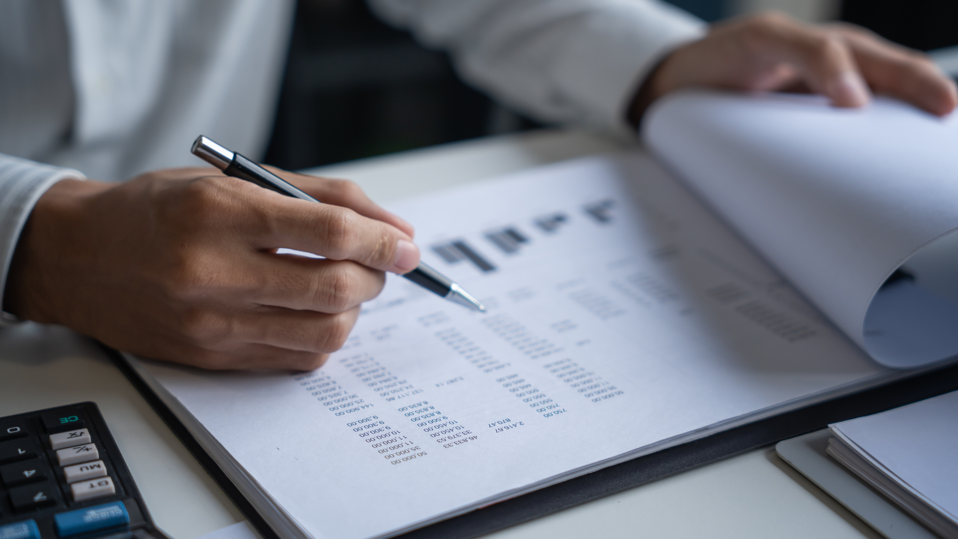 Person reviewing financial documents with a pen in hand, focused.