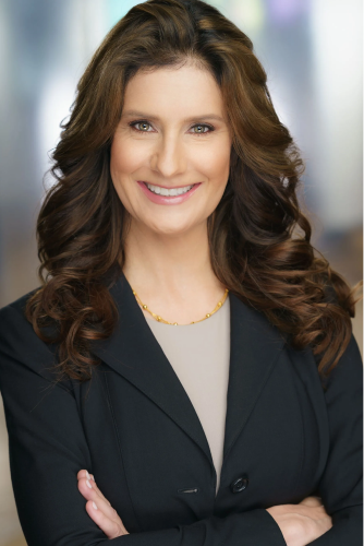 A woman in a black jacket is smiling with her arms crossed