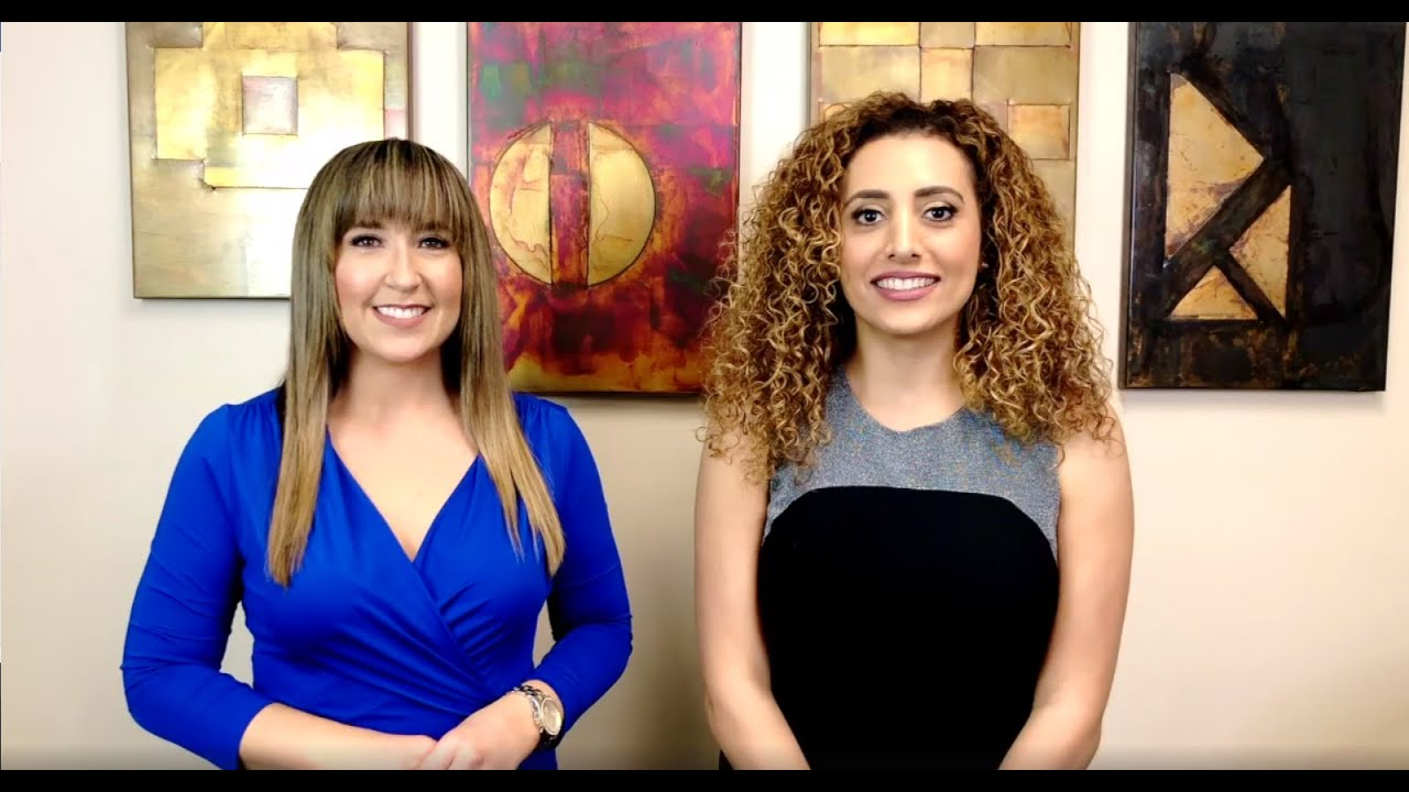 Two women are standing next to each other in front of paintings.