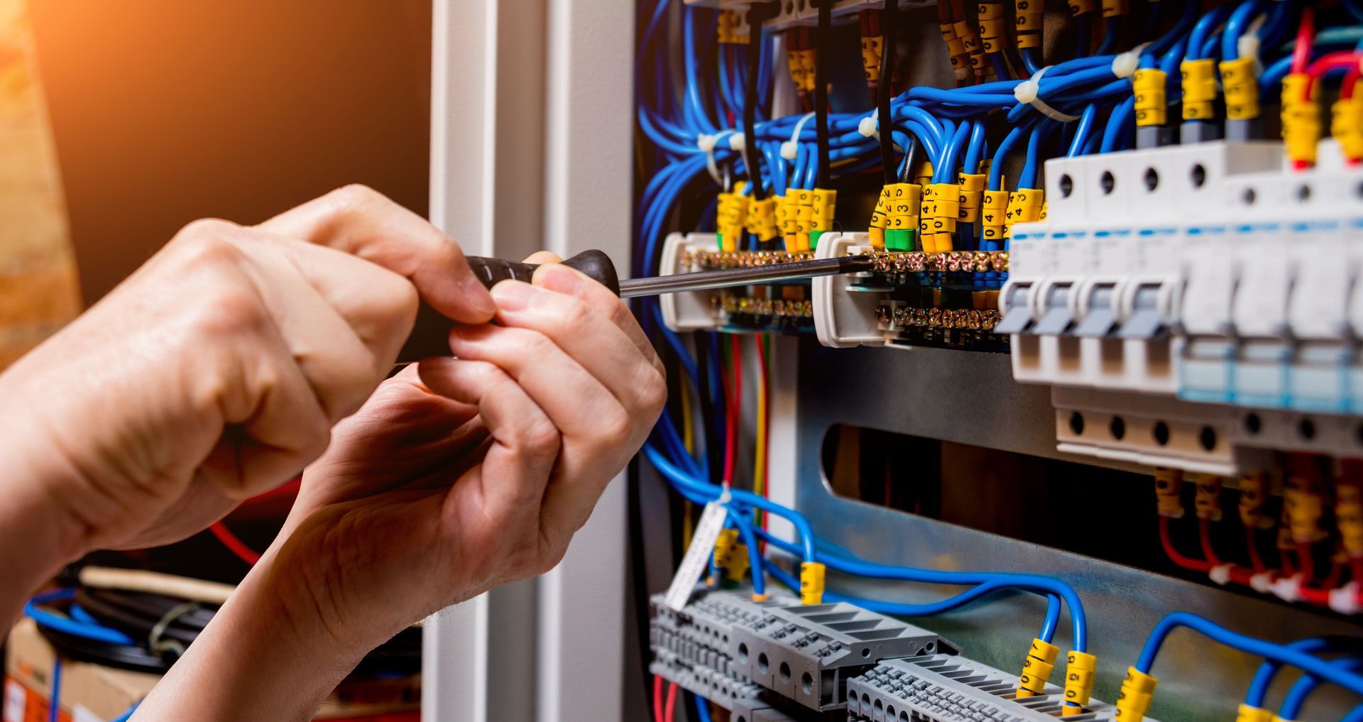 Hands of an electrician working on electrical panel, tightening screws, blue wires.