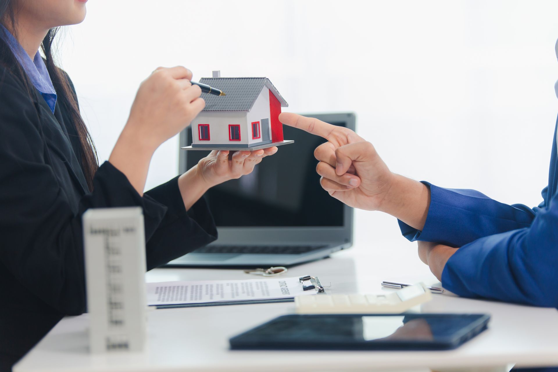 Real estate agent points to a model house while meeting with a client at a desk.