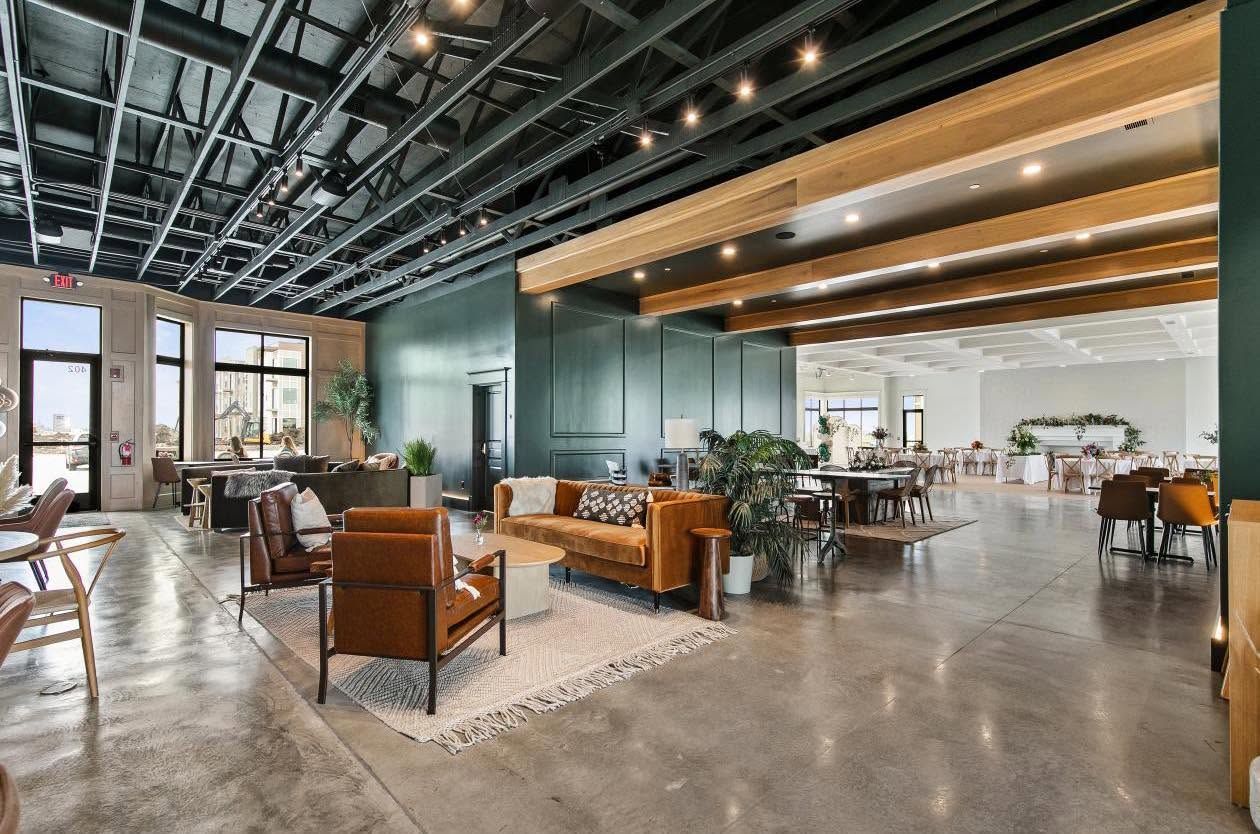 Bright event space with long white reception table, glass garage doors, and white floral decor
