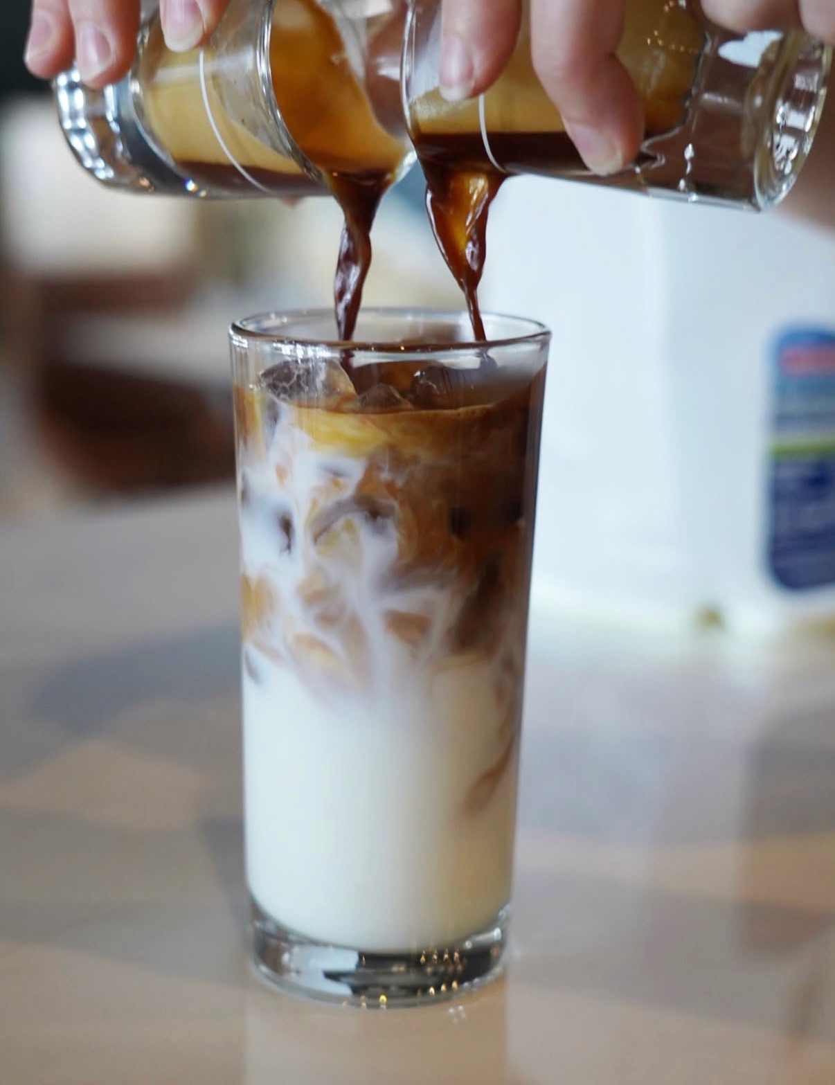 Hands pour coffee over ice into a glass of milk