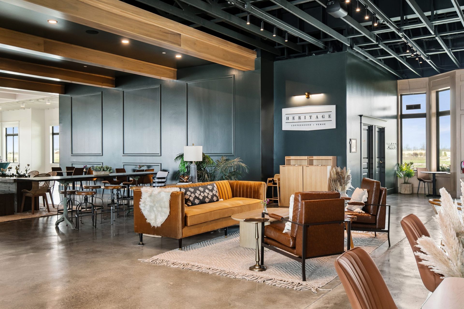 Modern lounge with sofas, dining tables, exposed beams, and large windows in a bright, airy interior