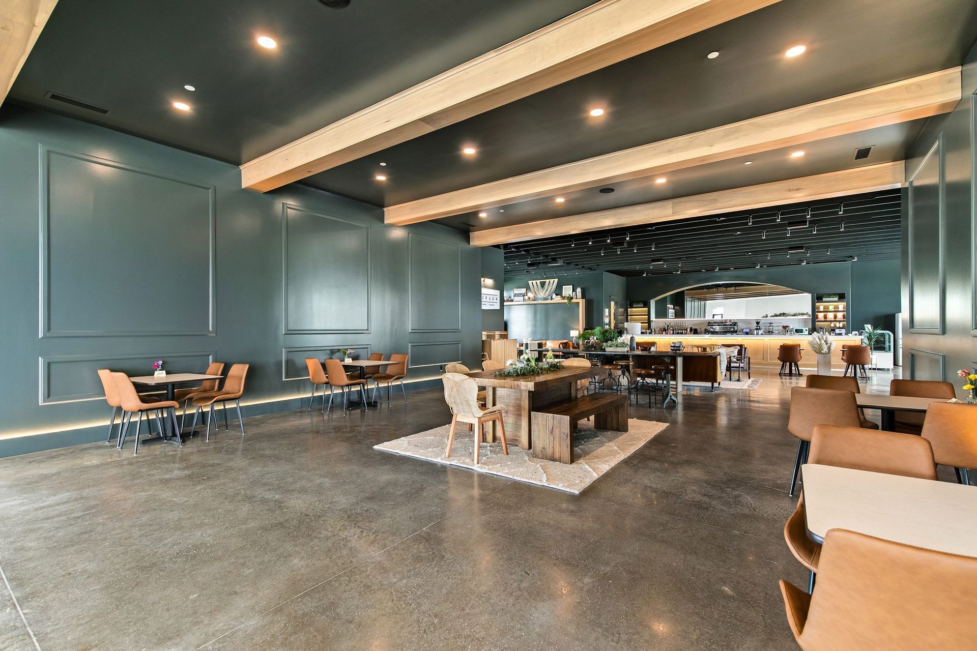 Modern lounge with teal walls, polished floor, central seating, and a bar area in the background