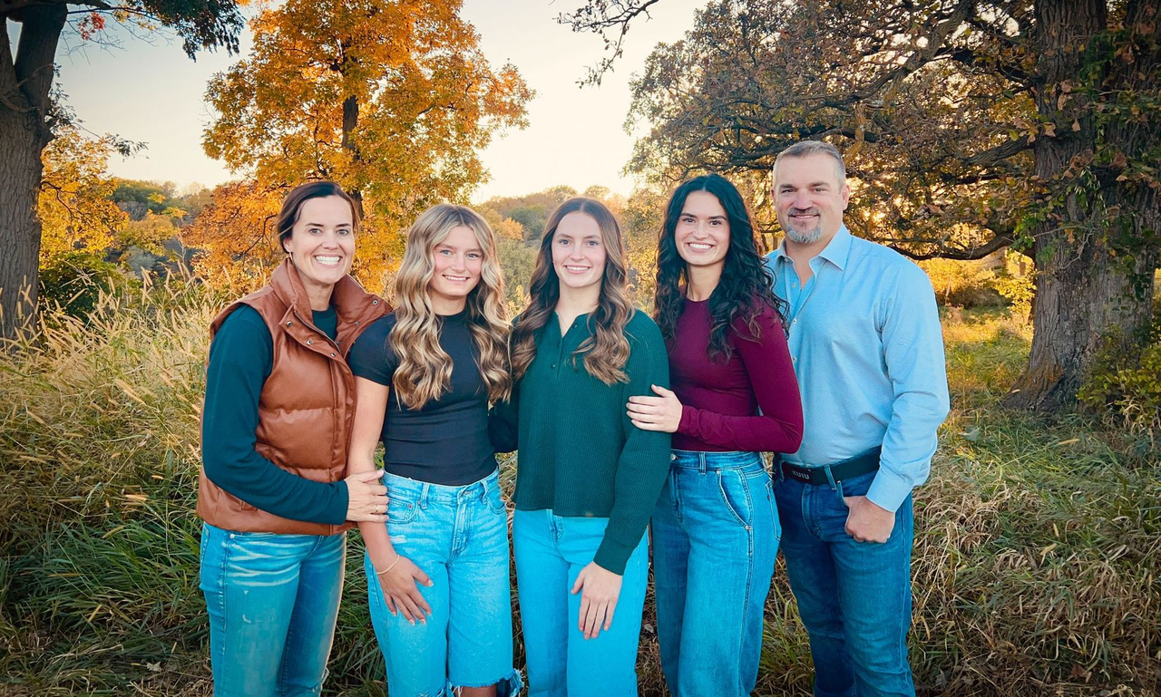 Five people standing together outdoors in front of autumn trees, smiling at the camera.