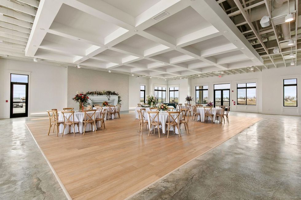 Bright event hall with wooden dance floor, round tables, white chairs, and large windows