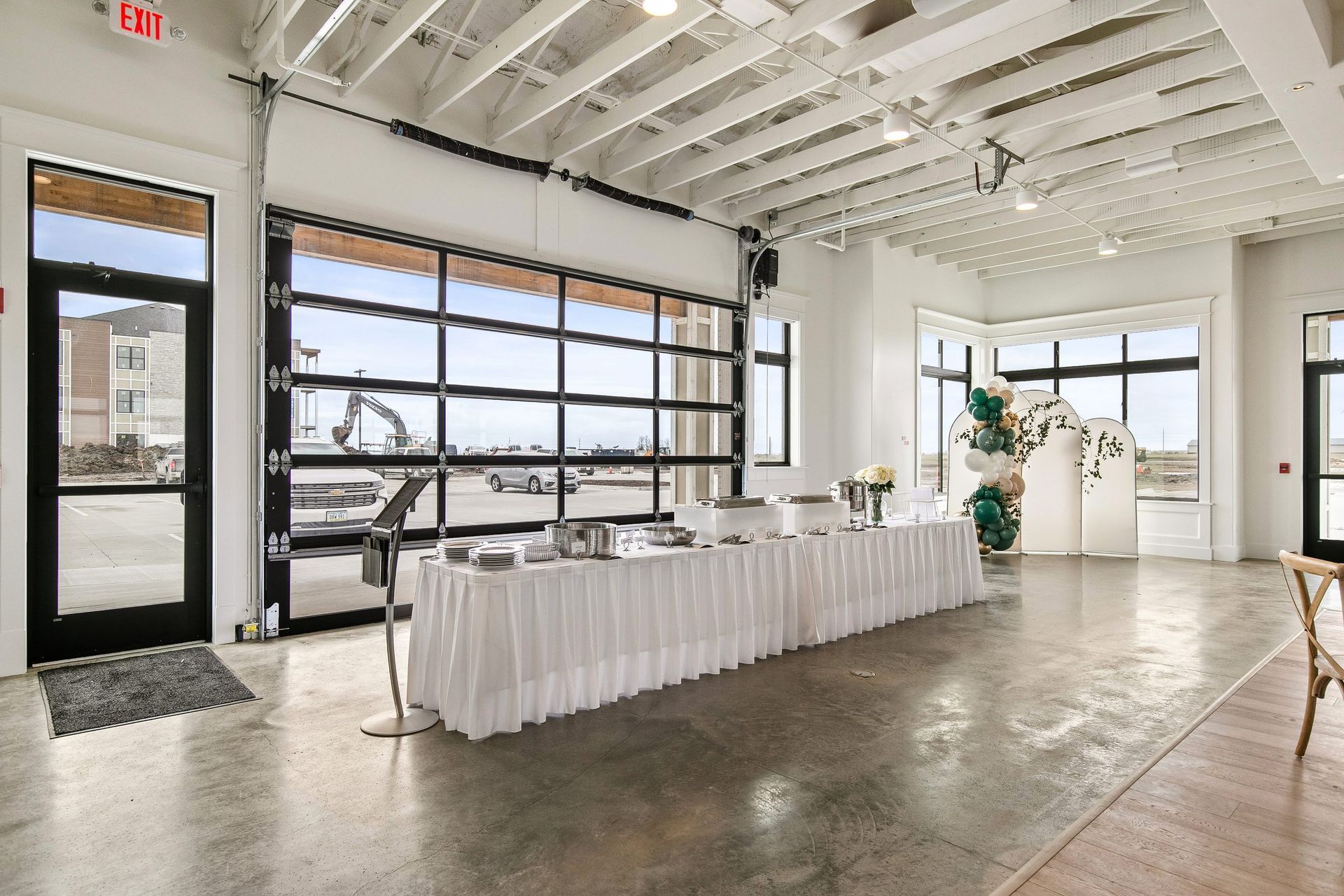 Bright loft event space with long white buffet table, large windows, and industrial garage doors