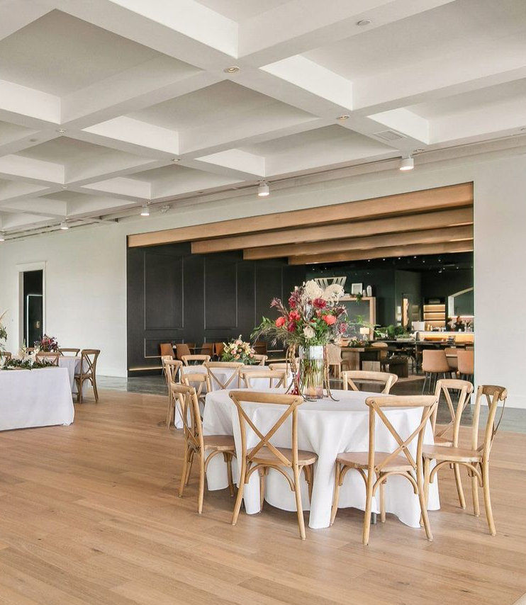 Elegant banquet hall with round tables, white linens, wooden chairs, and floral centerpieces