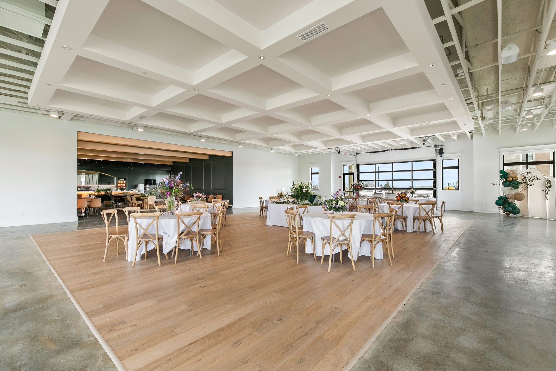 Bright modern event hall with round tables, white chairs, wood floors, and large windows