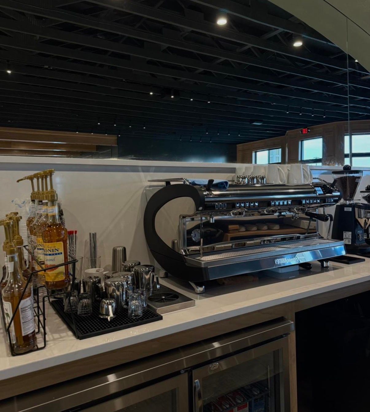 Coffee station with espresso machine, cups, and bottles on a counter in a modern café interior