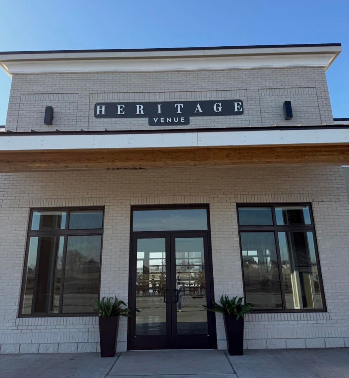 Storefront with a white brick facade and glass entrance, labeled “HERITAGE VILLAGE” above the door.