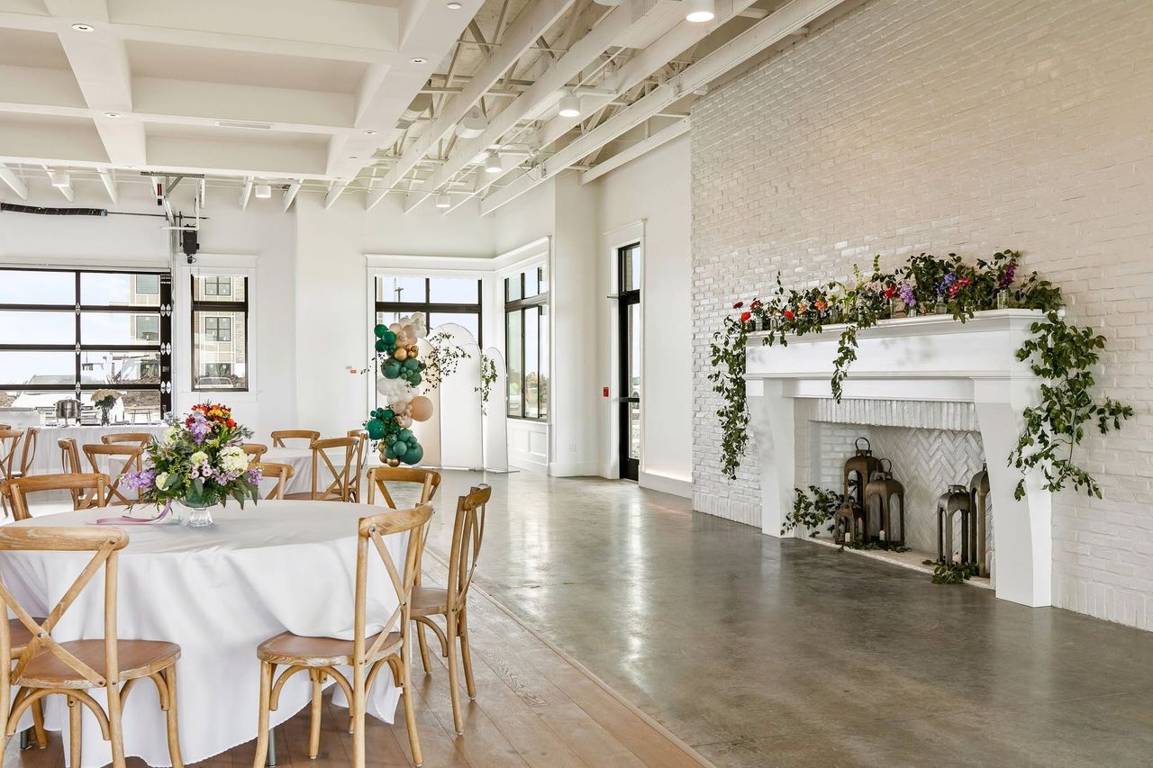 Bright event space with long white reception table, glass garage doors, and white floral decor