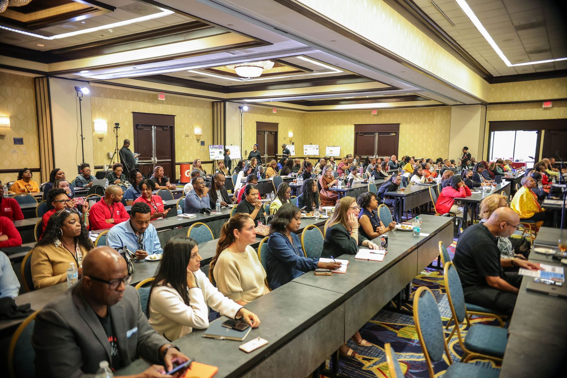 Conference room filled with attendees seated at long tables during a meeting or presentation.