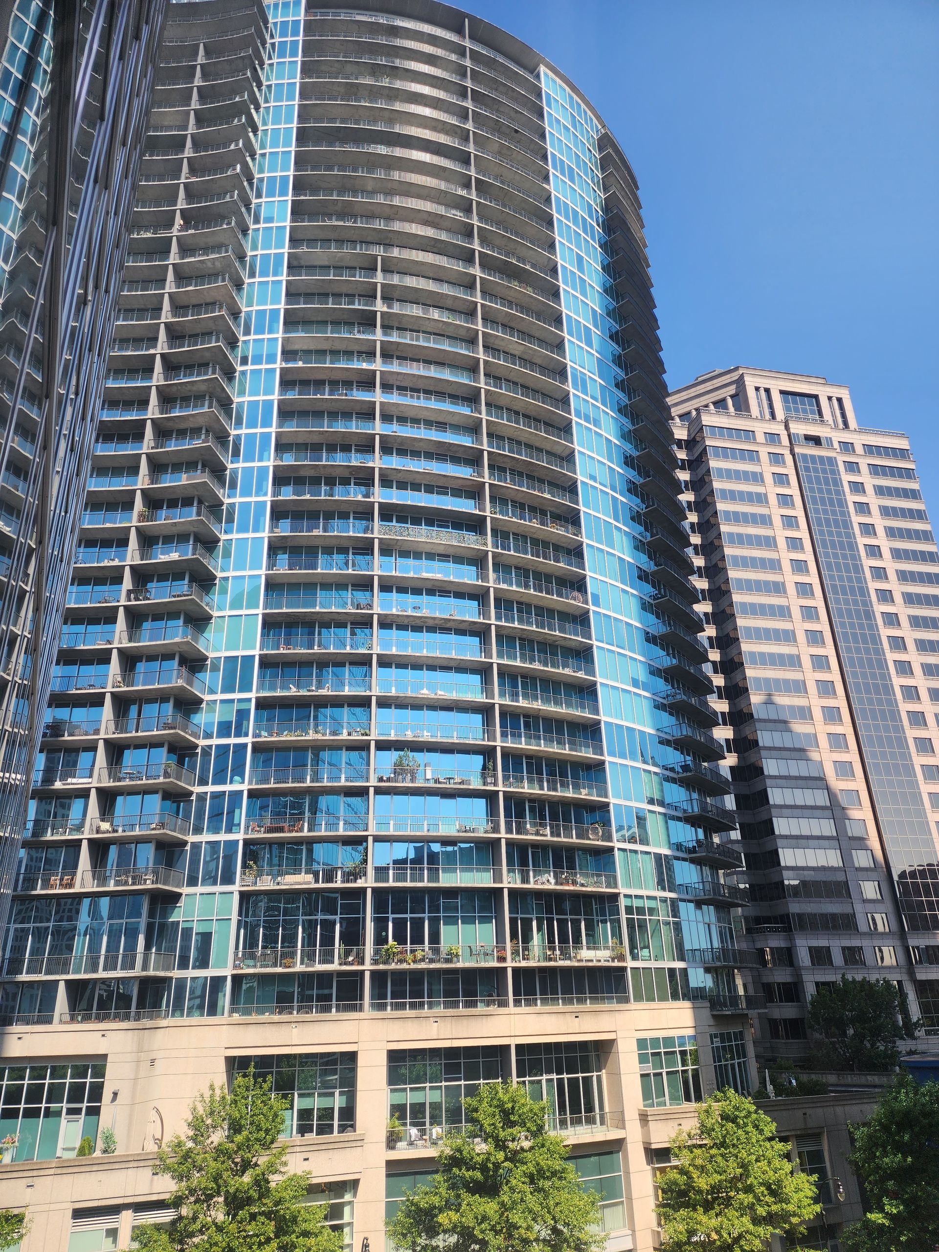 Two tall modern buildings with blue glass and balconies against a clear sky.