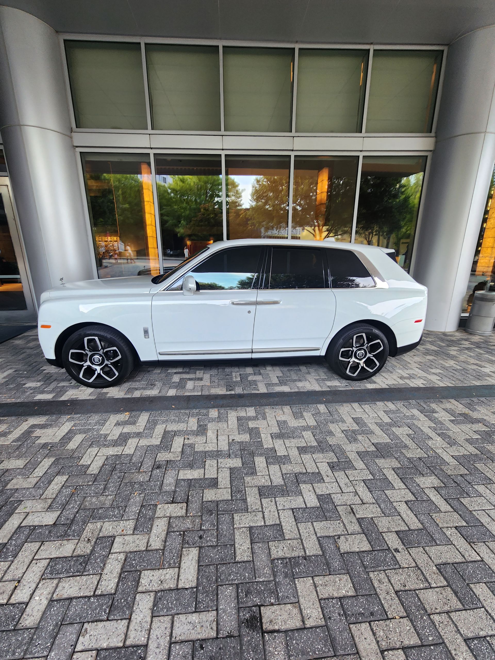 White Rolls Royce SUV parked on a patterned brick driveway under a building entrance.