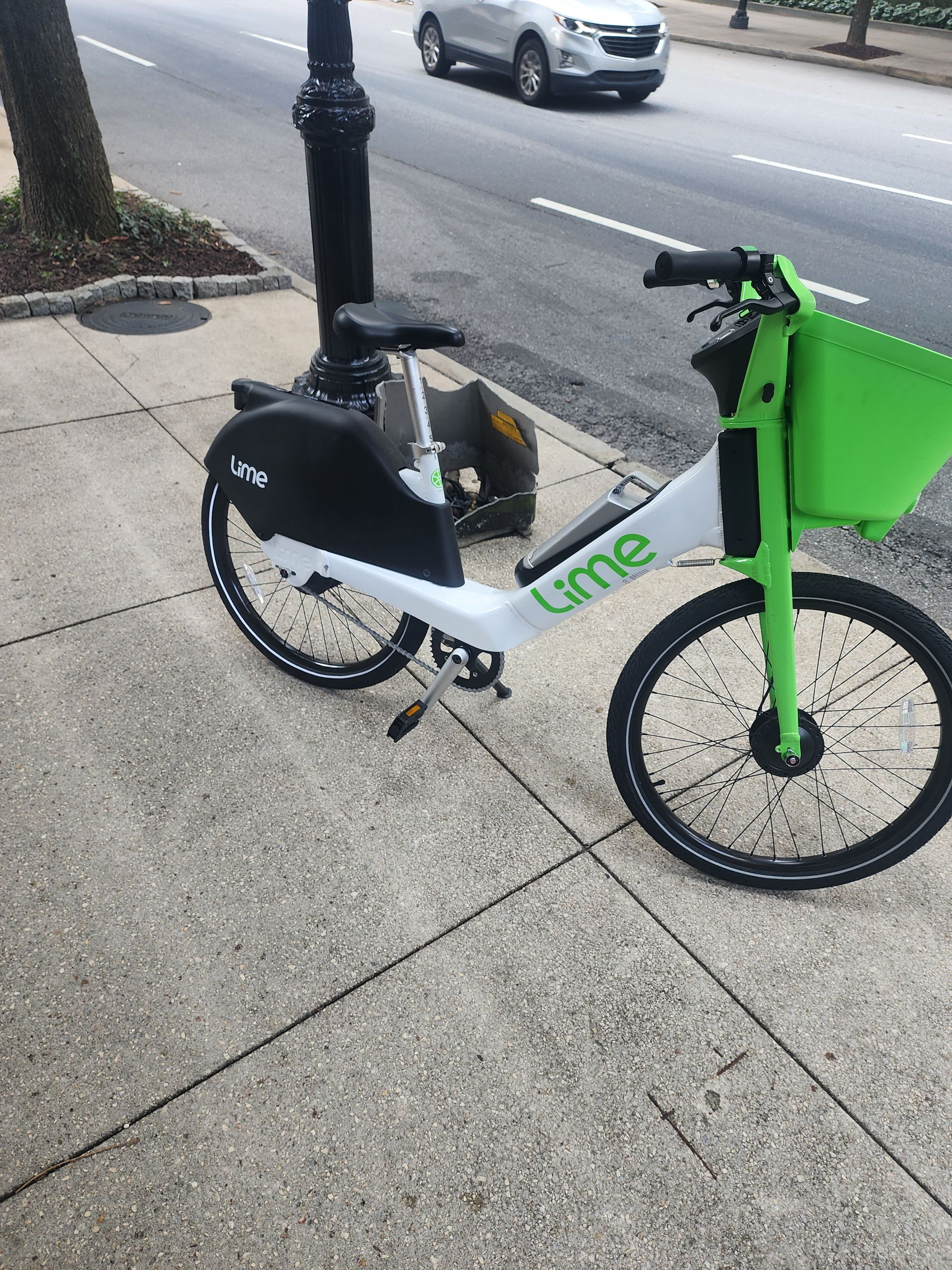 Lime electric bike on a sidewalk, next to a street with a car.