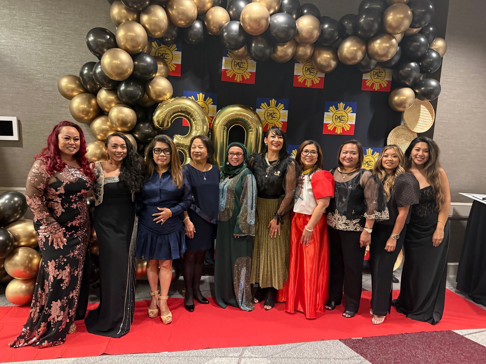 Group of people posing for photo at a formal event, red carpet, gold and black balloons,
