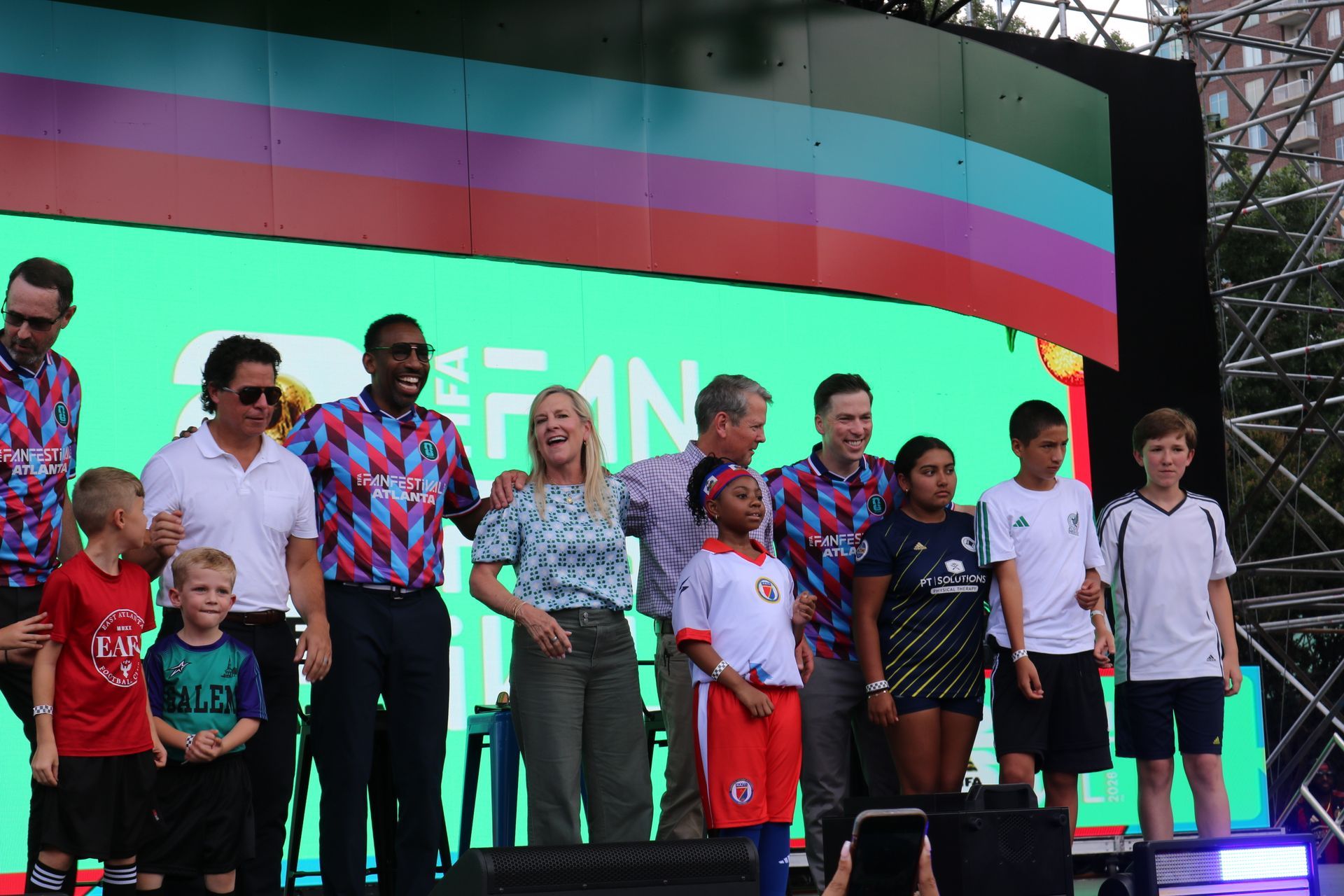 Group of people standing on a stage in front of a large colorful screen, posing for a photo.