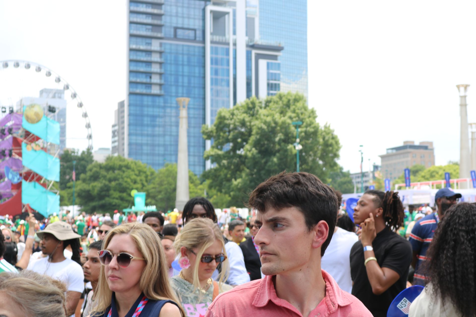 Crowd gathered at an outdoor festival with a Ferris wheel and tall city buildings in the background
