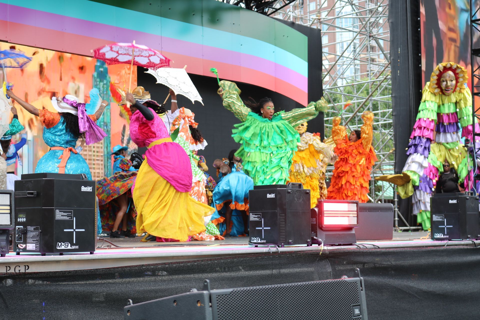 Colorful dancers in bright costumes performing on an outdoor stage with an arched backdrop