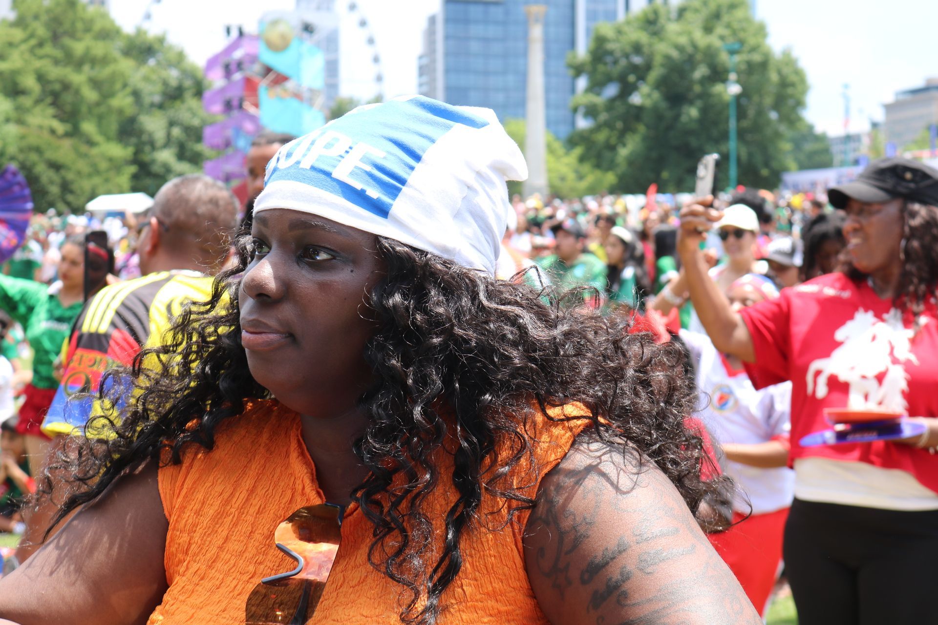 Crowd at outdoor festival, with a woman in orange and blue headwrap in the foreground