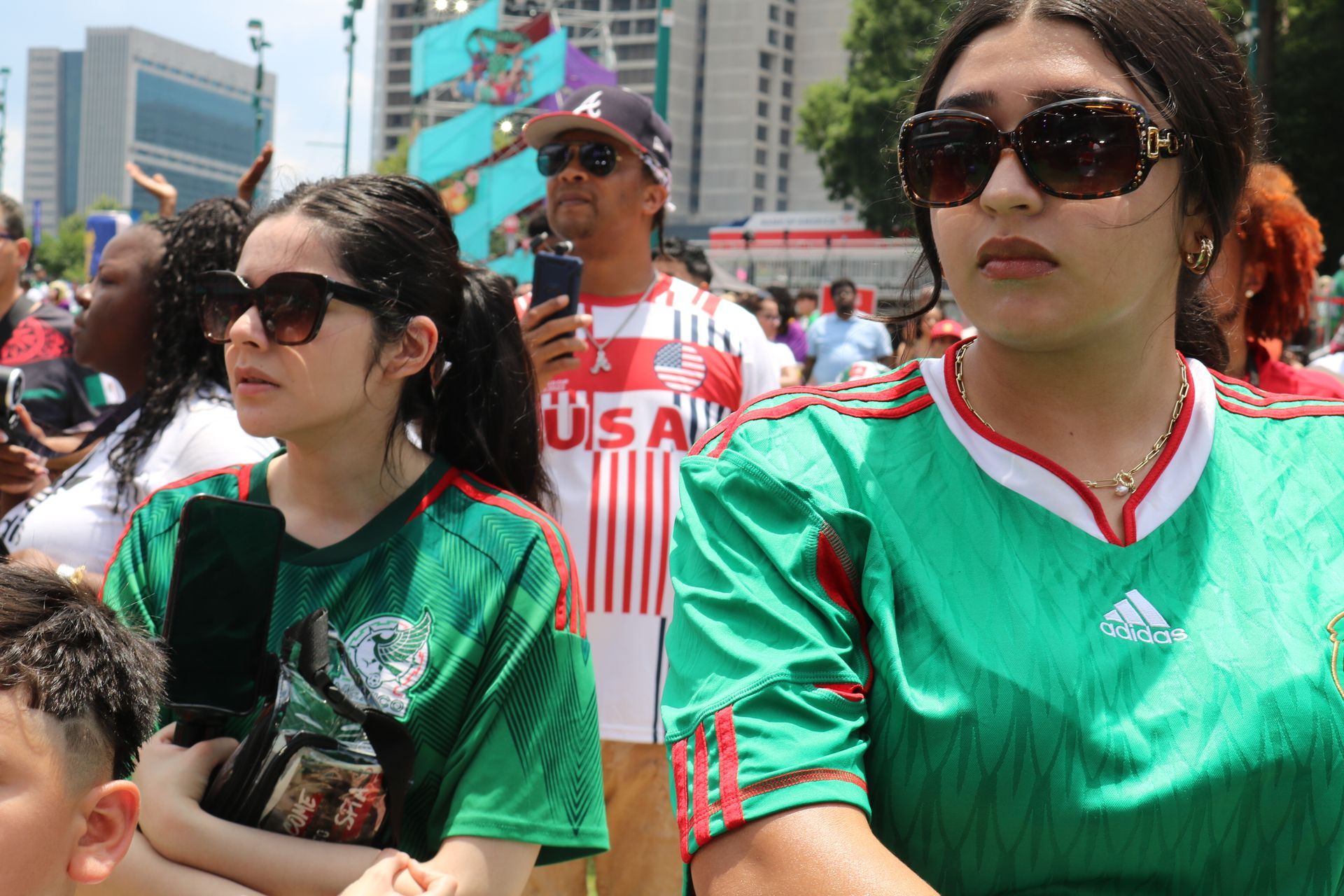 Crowd at outdoor event, two people in green jerseys and sunglasses in the foreground