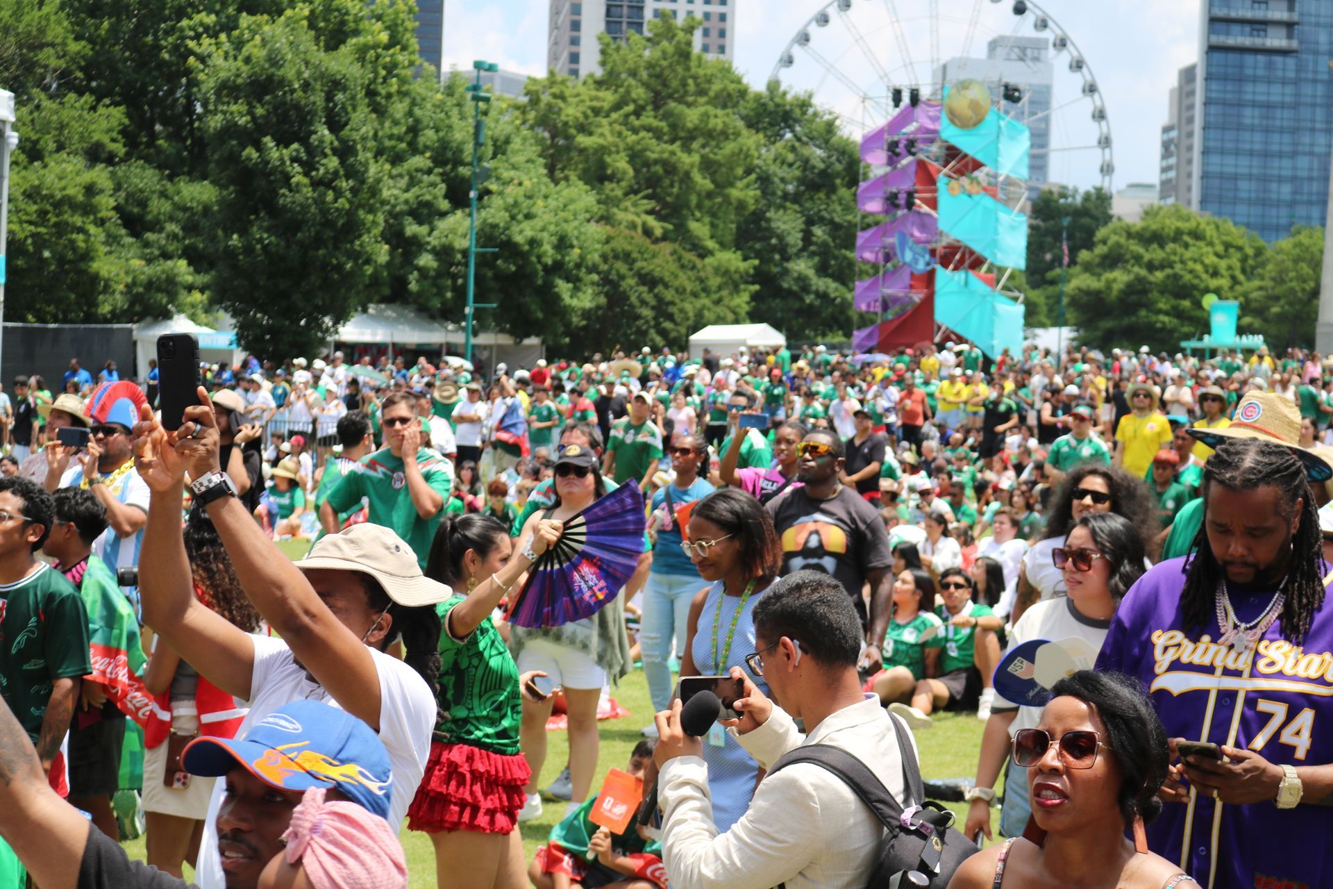 Crowded outdoor festival with people dancing, raising hands, and colorful decorations in a park