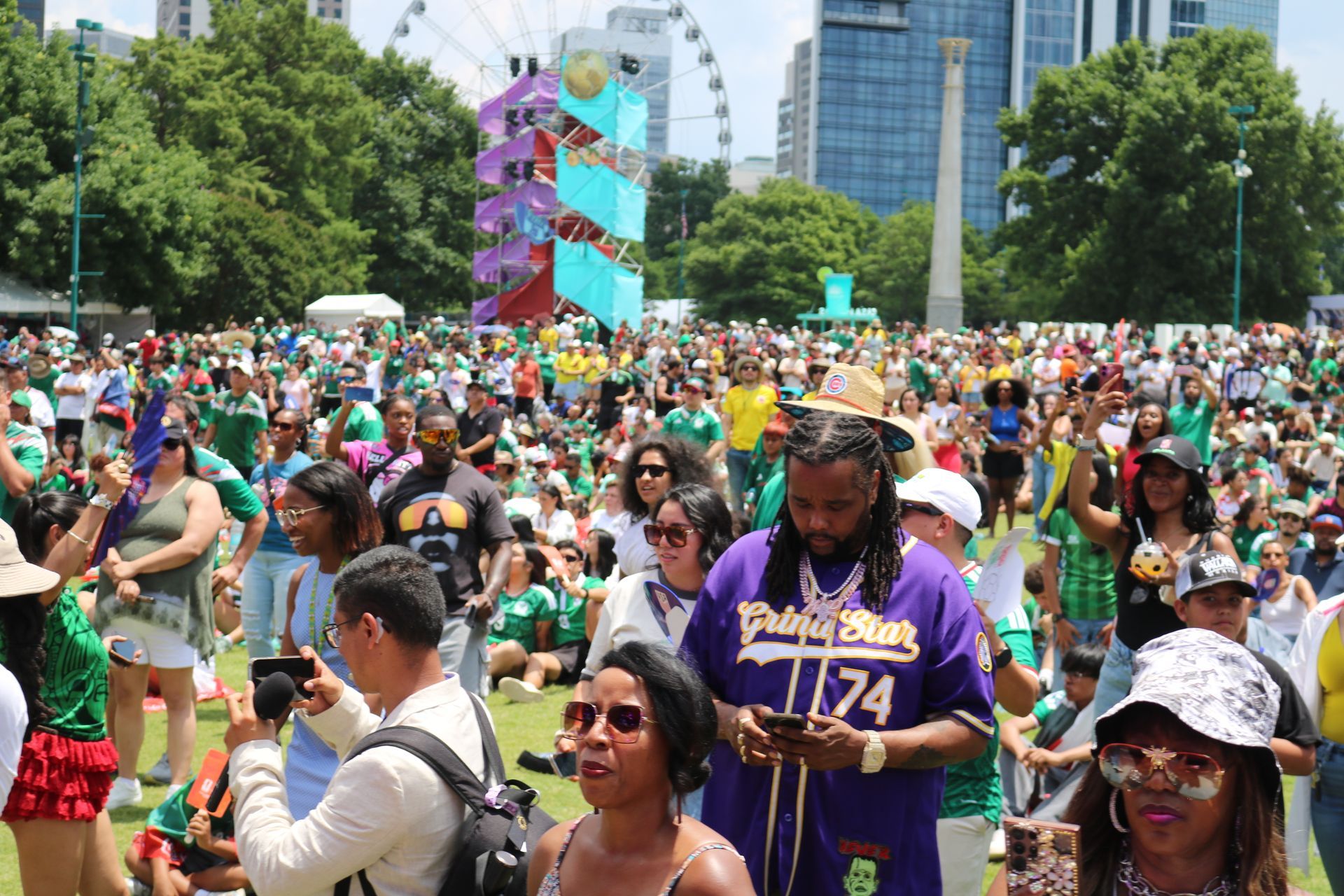Crowded outdoor festival with people dancing, colorful flags, and a Ferris wheel in the background