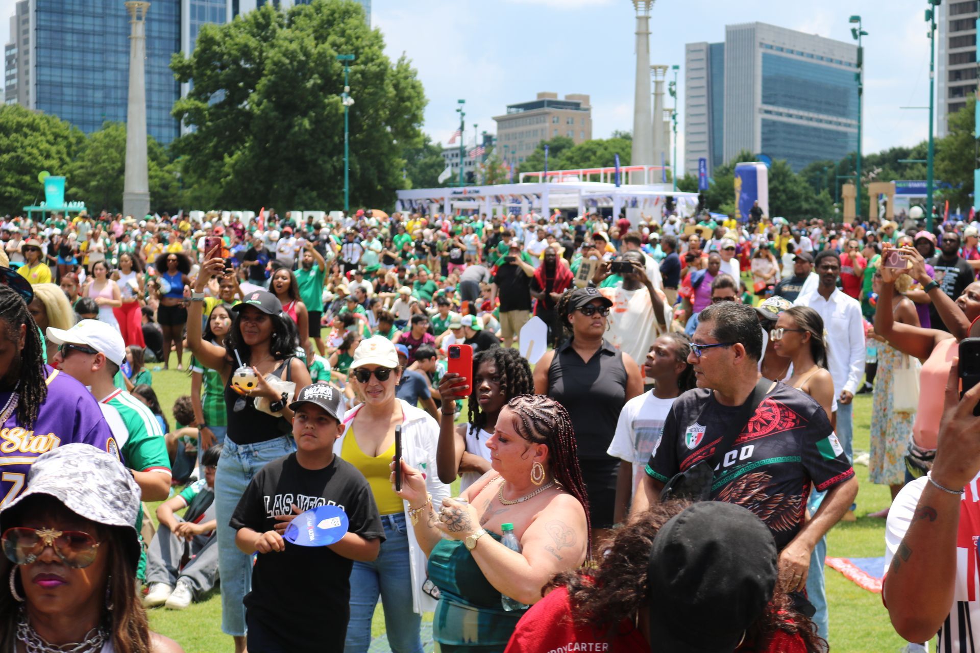 Crowd gathered outdoors at a city rally, with people holding signs in front of tall buildings.