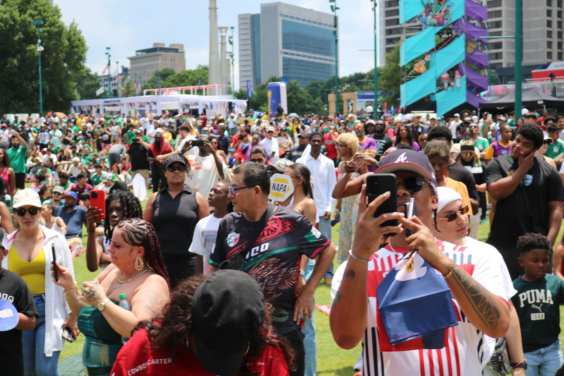 Crowded outdoor parade with people taking photos and colorful flags in a city plaza