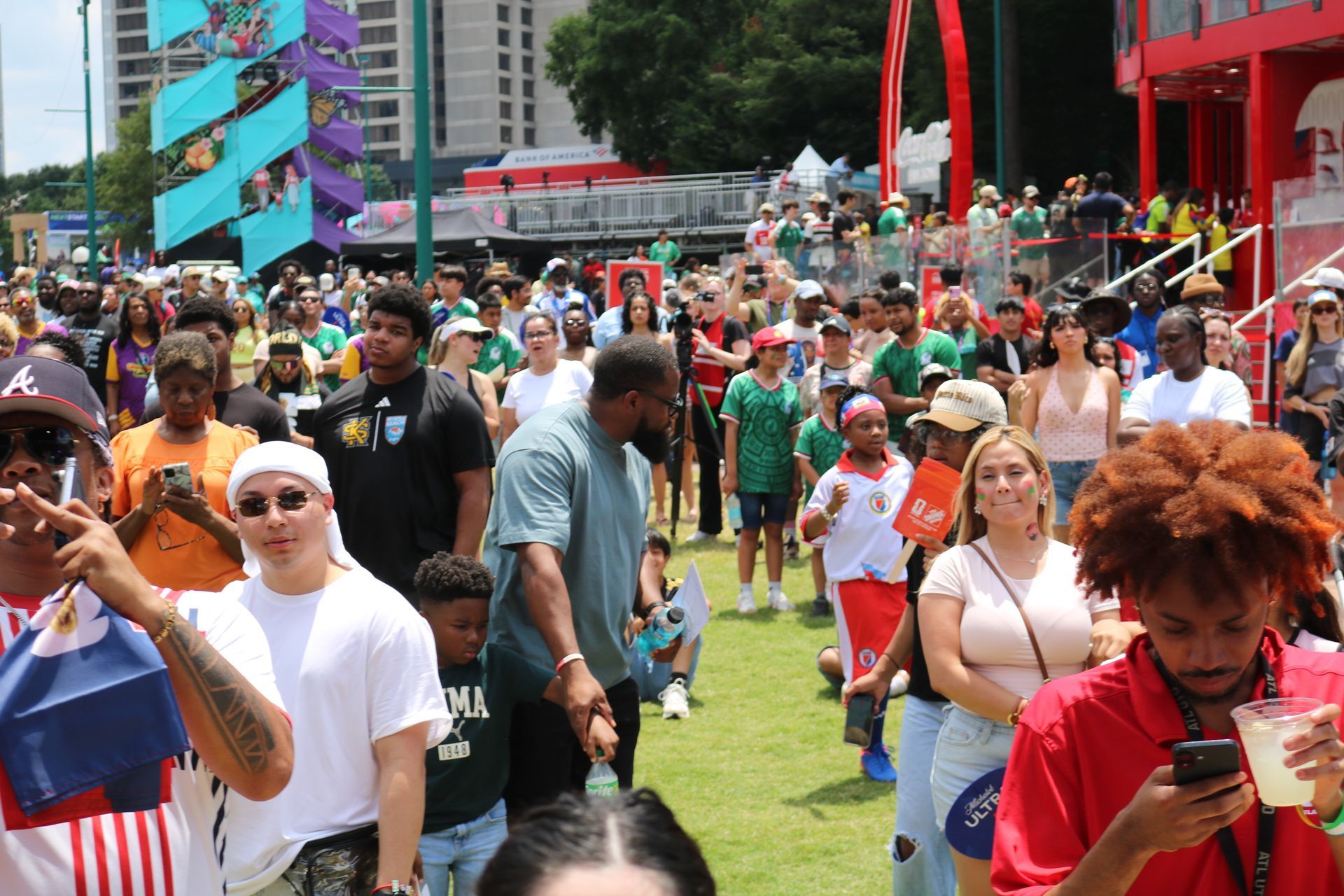Crowded outdoor festival on a grassy city plaza with people walking, taking photos, and colorful decorations