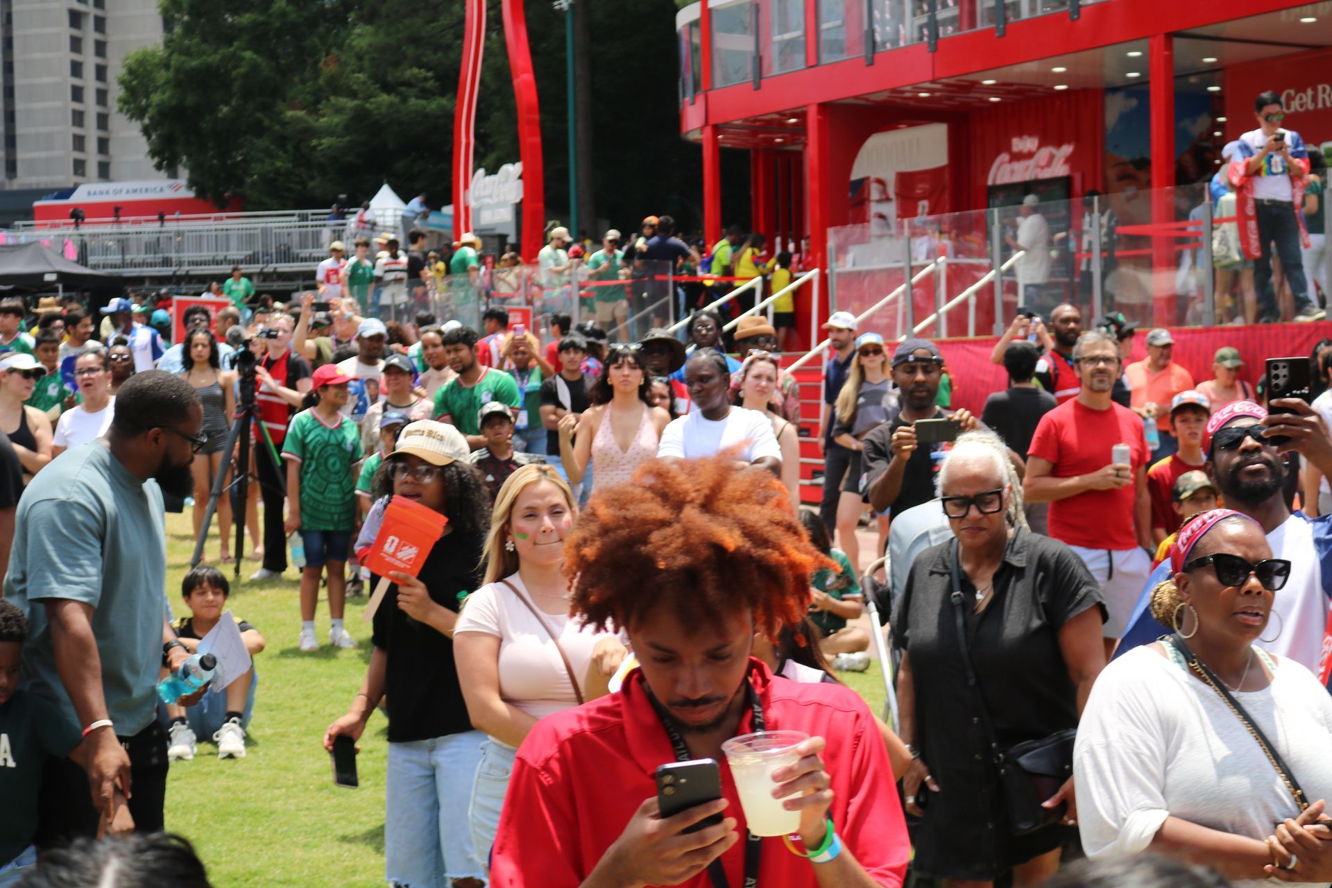 Crowd gathered outside a red building at a lively outdoor event, with people holding drinks on a grassy lawn