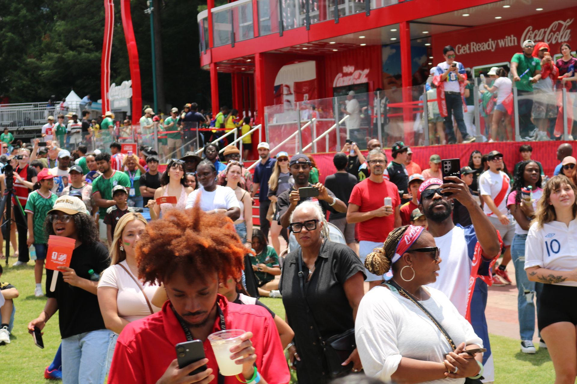 Crowded outdoor event with people in festive costumes near a red building and grassy lawn