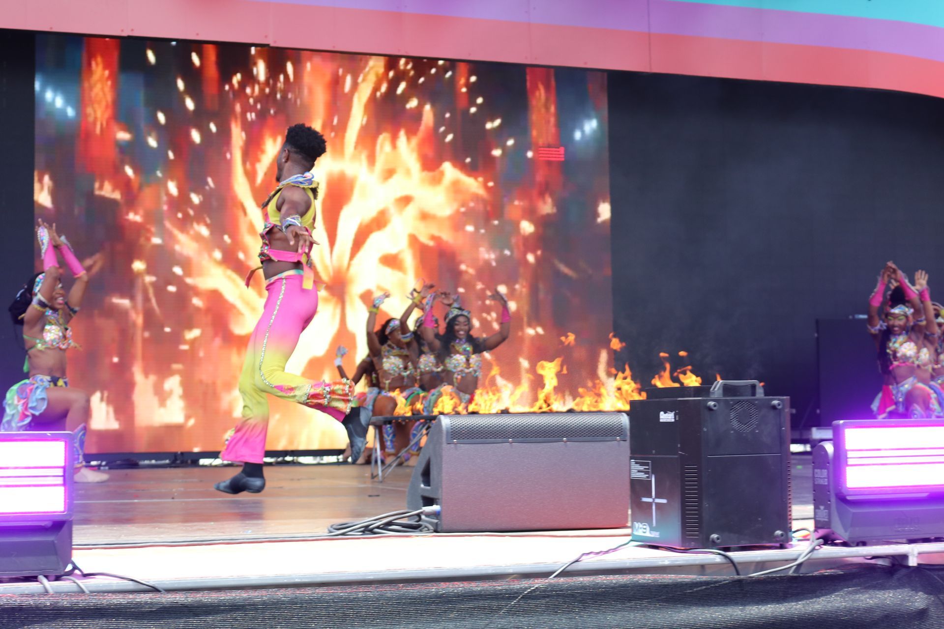 Performers on a stage with bright orange flames and colorful lights during a live show