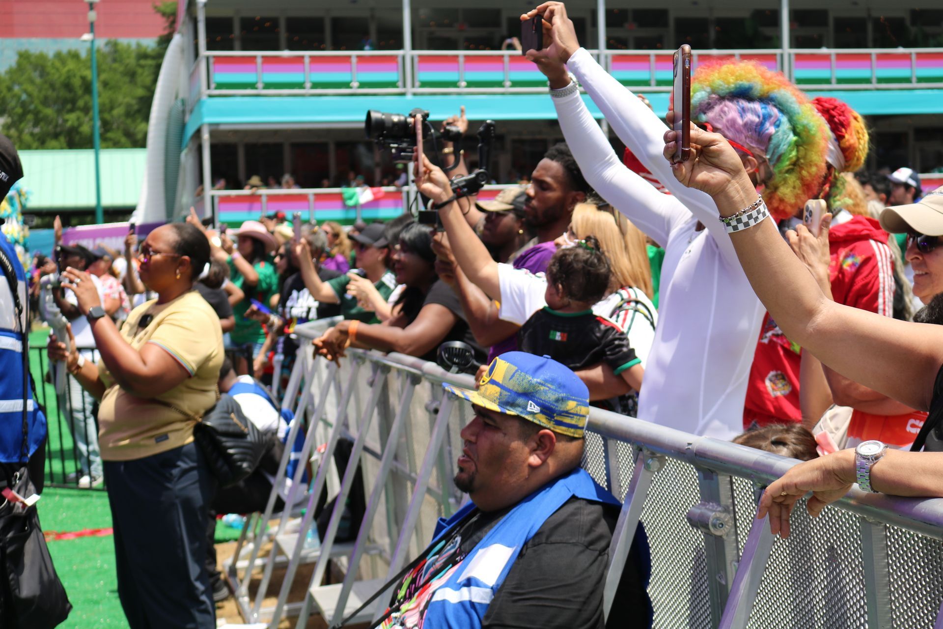 Crowd cheering behind a metal barrier, with people raising hands and phones at an outdoor event
