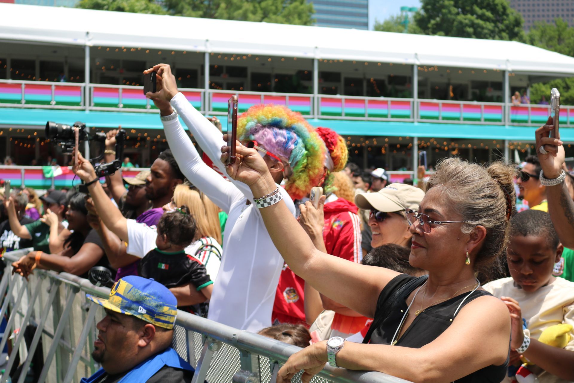 Crowd cheering and raising hands at a colorful outdoor parade in front of stadium seating