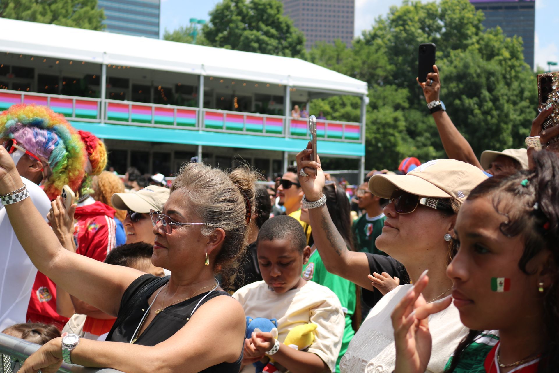 Crowd cheering at an outdoor parade, with people raising hands and colorful costumes in the background
