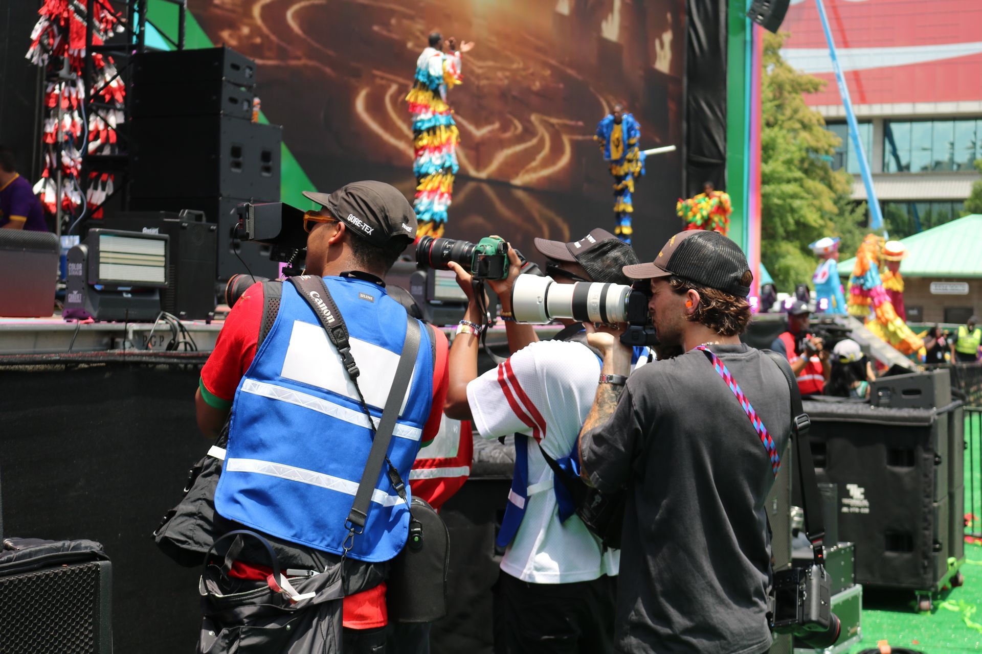 Photographers filming a stage performance, with large cameras and colorful lights in the background