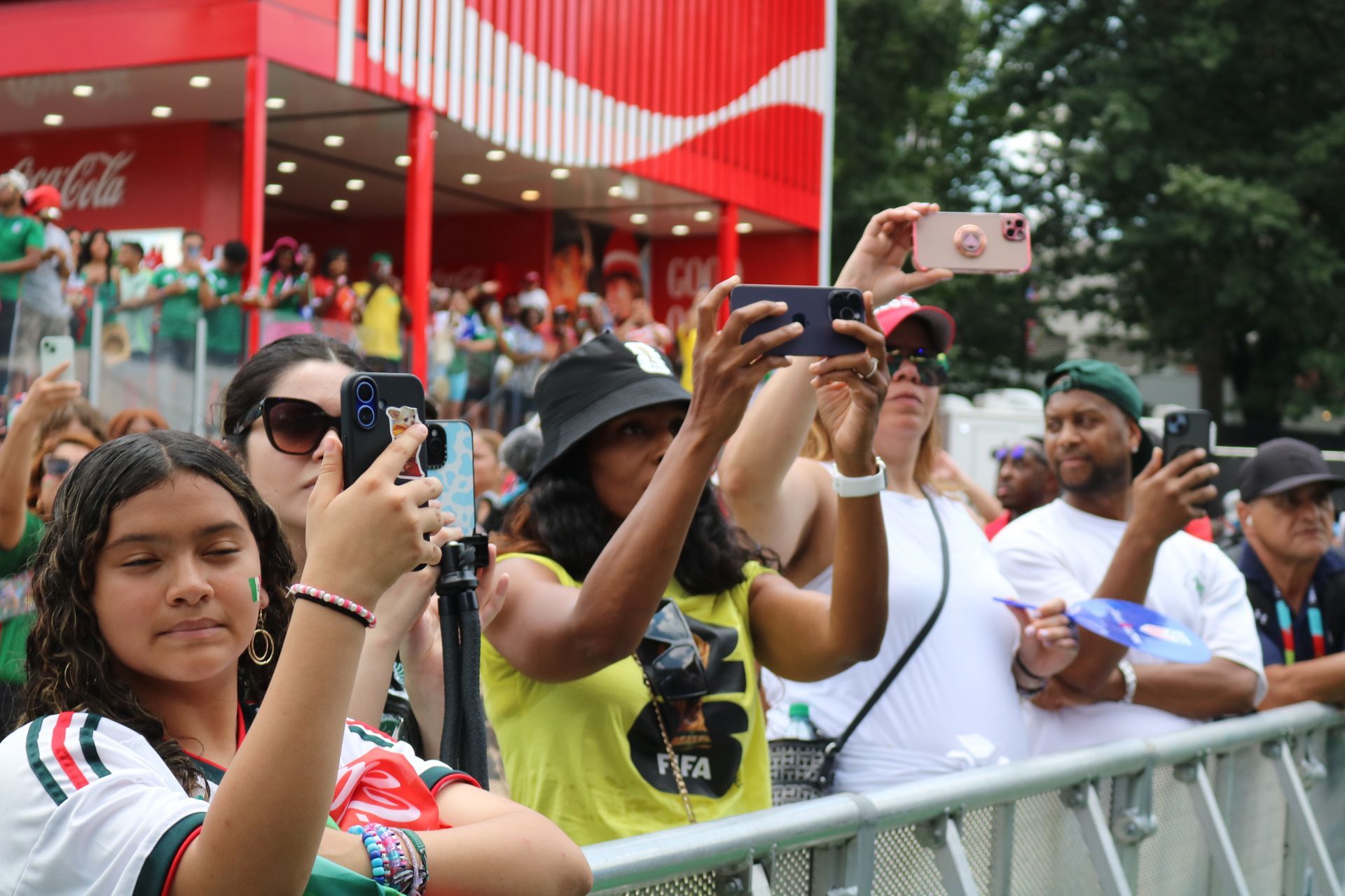 Crowd at a barrier taking photos and cheering at an outdoor event under a red canopy