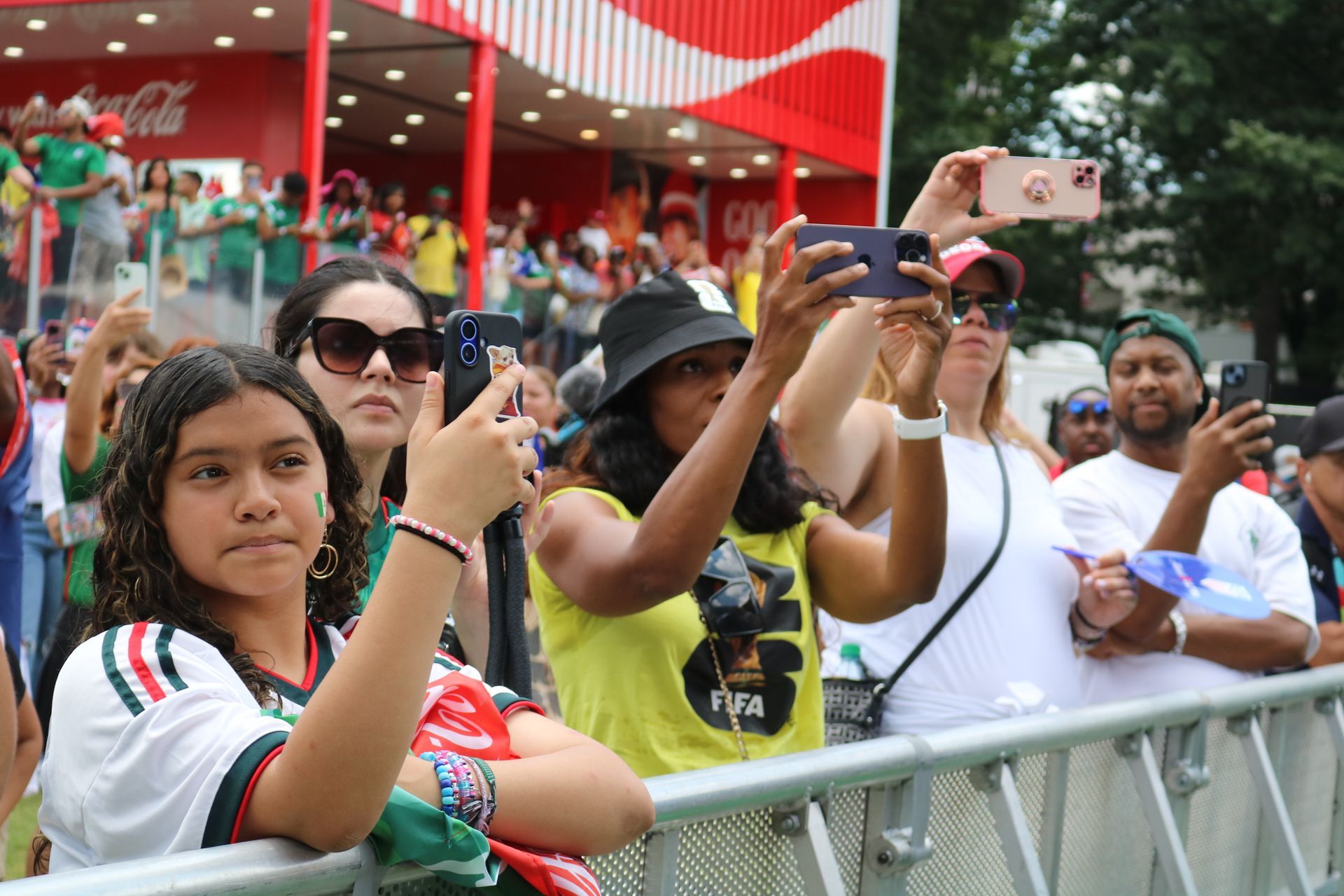 Crowd behind metal barricade taking photos at an outdoor event with a red building in the background