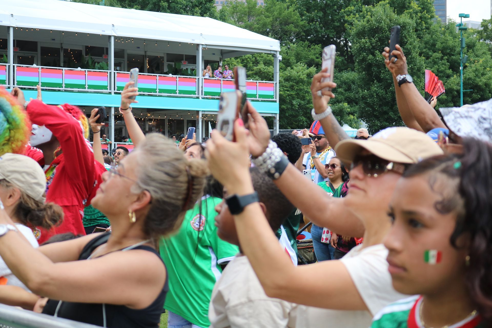Crowd cheering outdoors, raising hands and phones near a colorful parade float