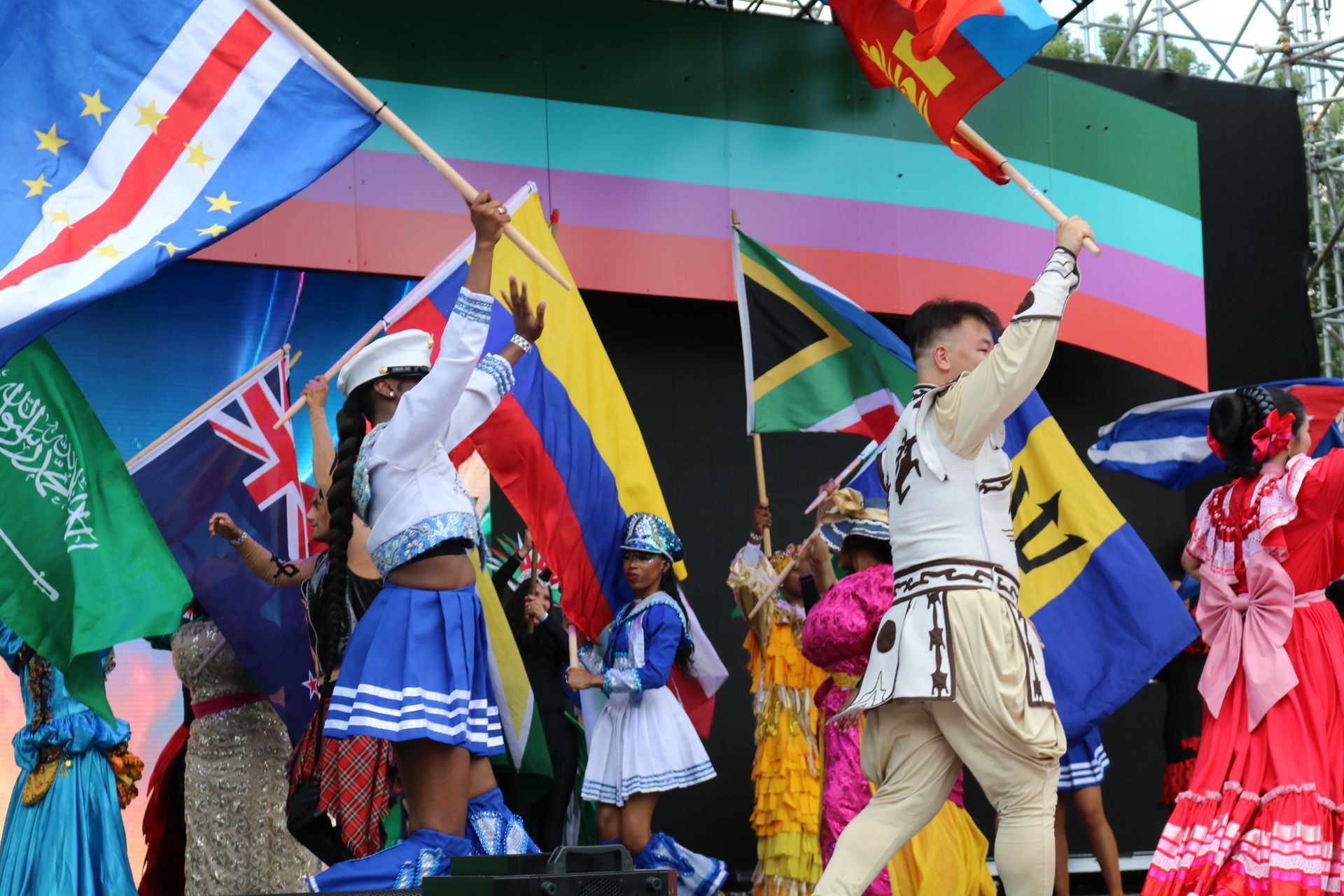 People waving colorful flags and dancing on a stage in traditional costumes