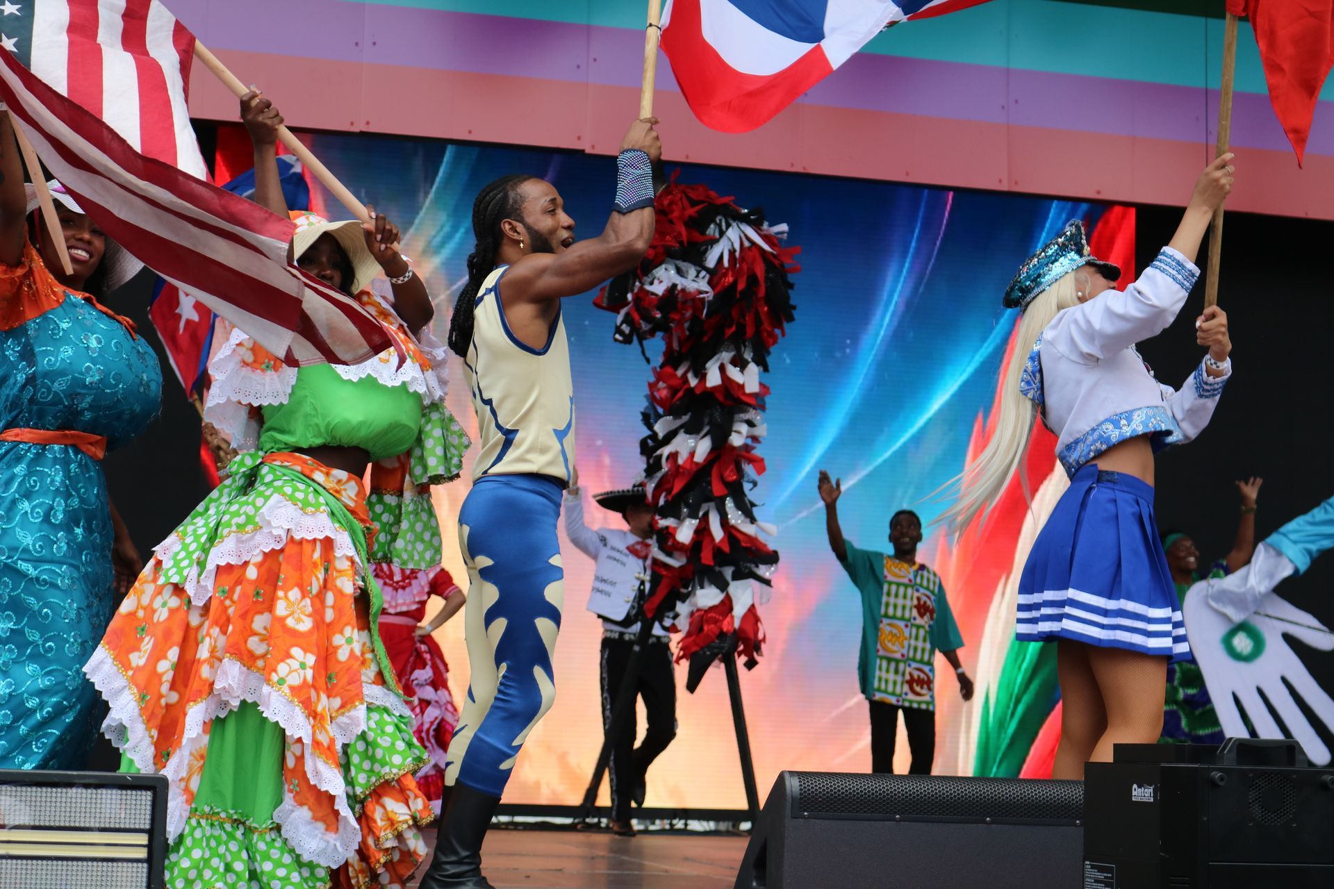 Performers in colorful costumes dancing onstage with flags and a bright backdrop