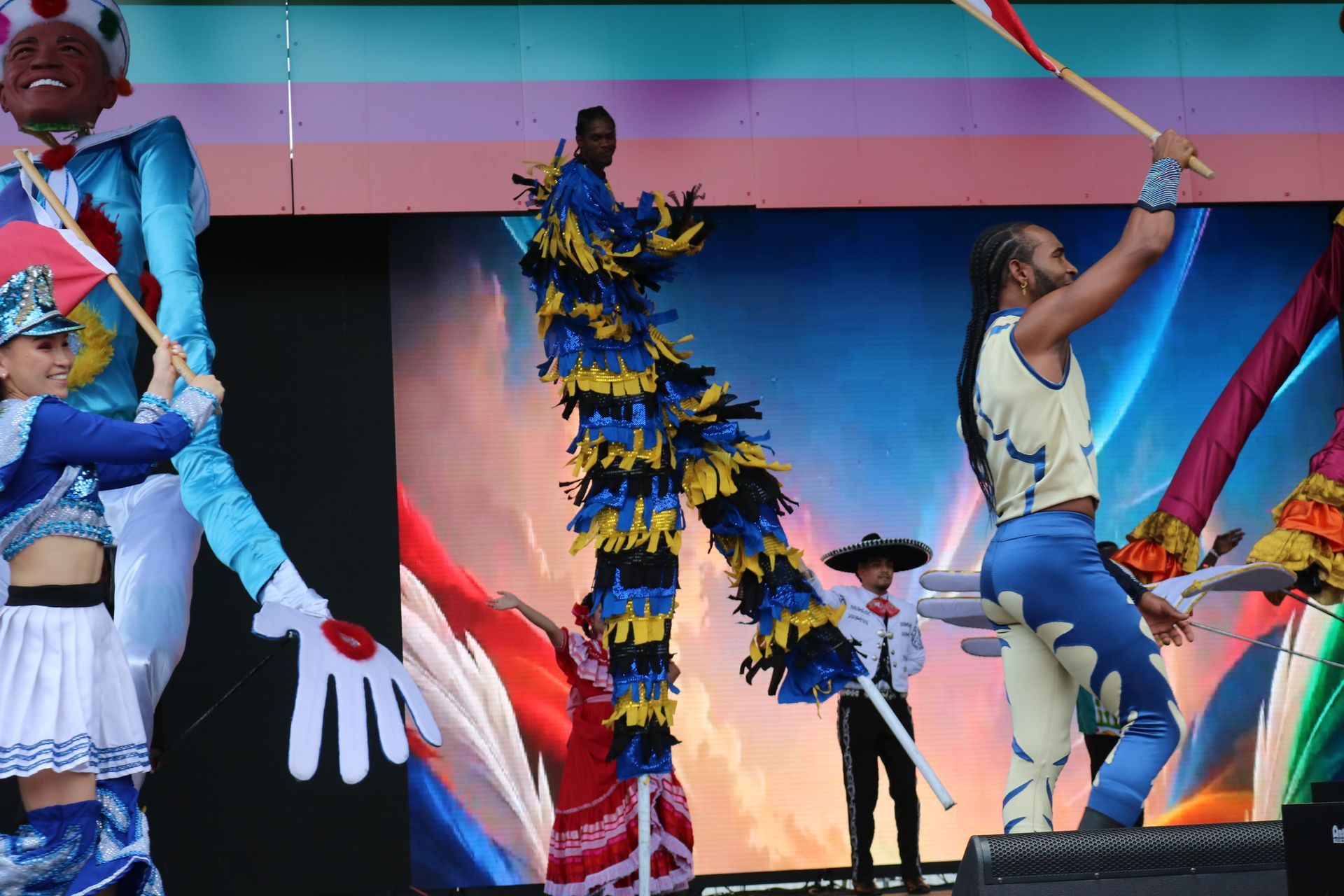 Stage performance with dancers in colorful costumes and a feathered tree-like prop under bright lights