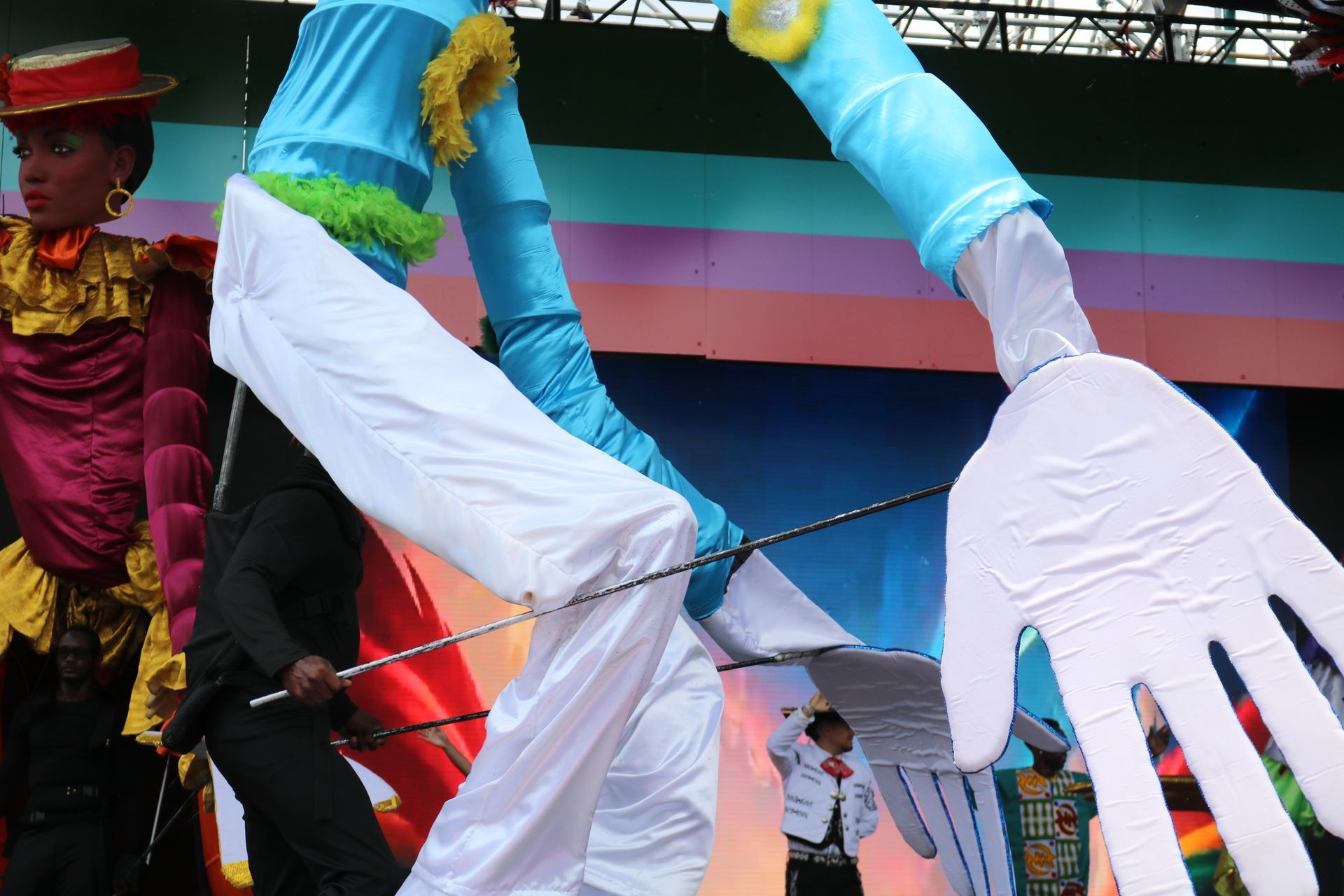 Large colorful parade figure with blue arms and white hands on a stage
