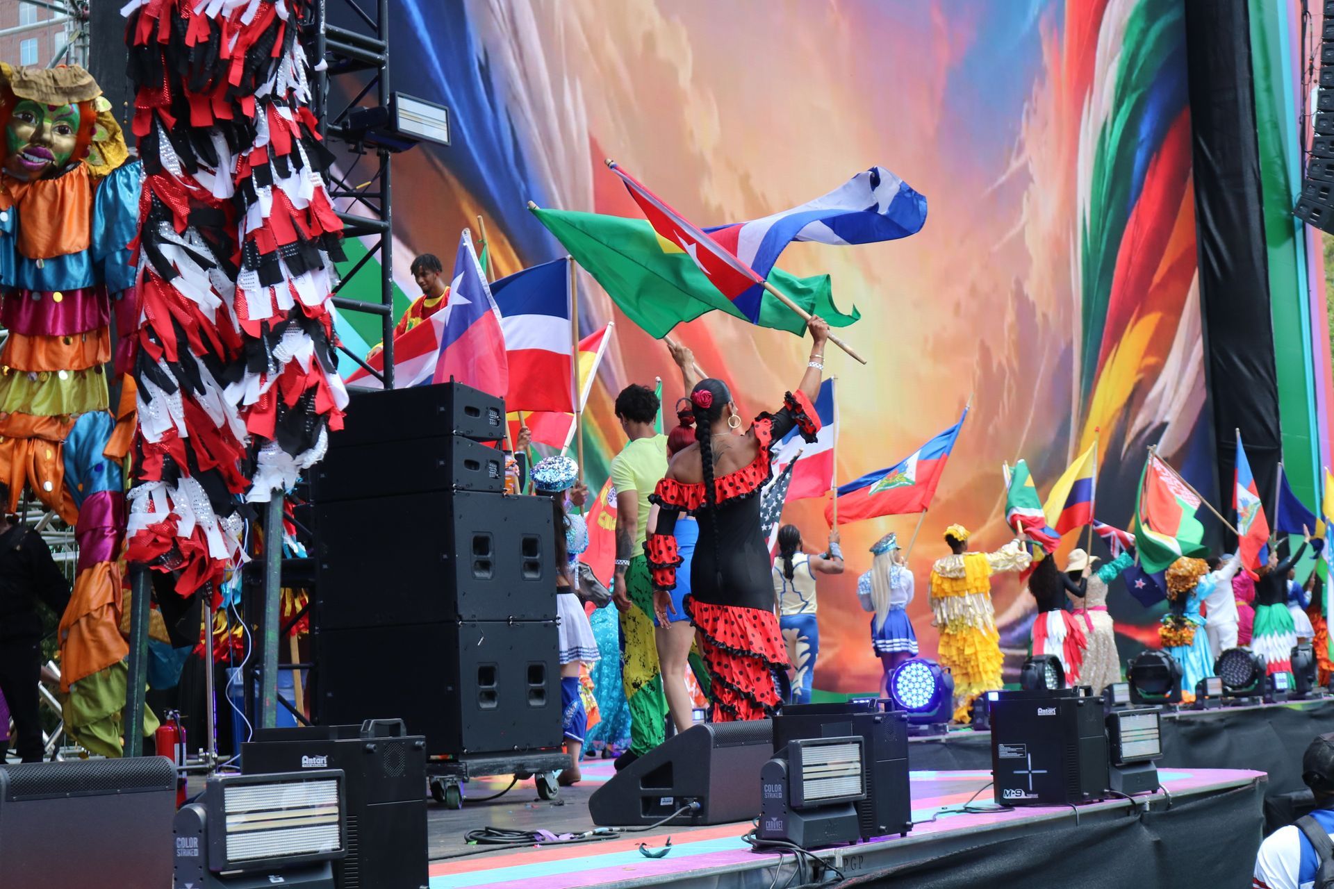 Colorful dancers on a stage with large flags and vibrant fabric backdrops at a festival performance