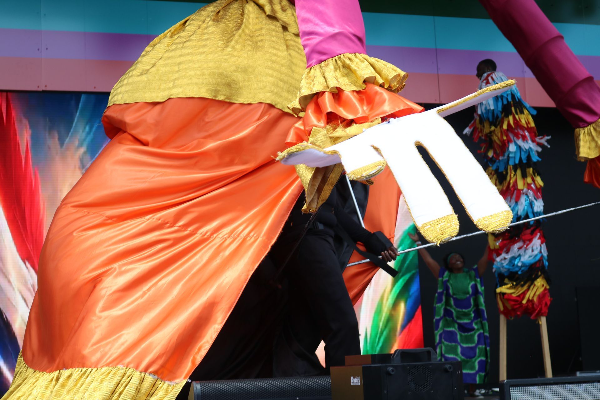 Person in a colorful costume performing on stage with orange and pink fabric and a white prop