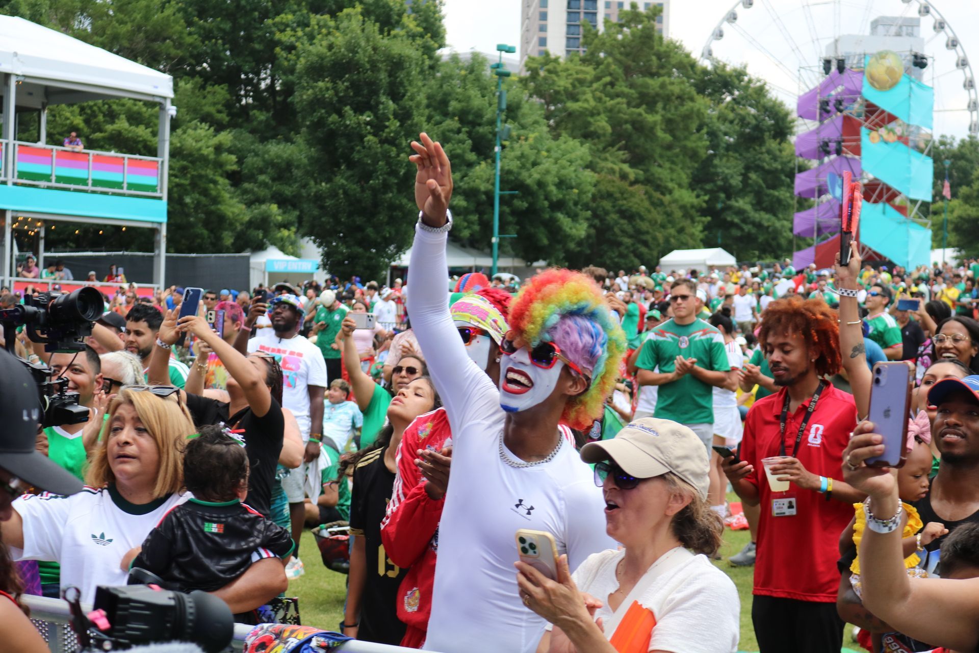Crowd celebrating at a pride parade, with a person in rainbow wig waving in the foreground
